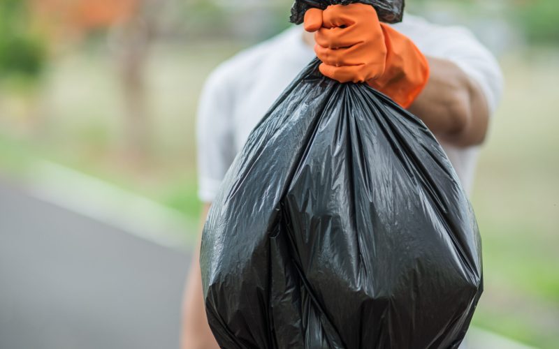 A man wearing orange gloves collecting garbage in a black bag. Selective focus.